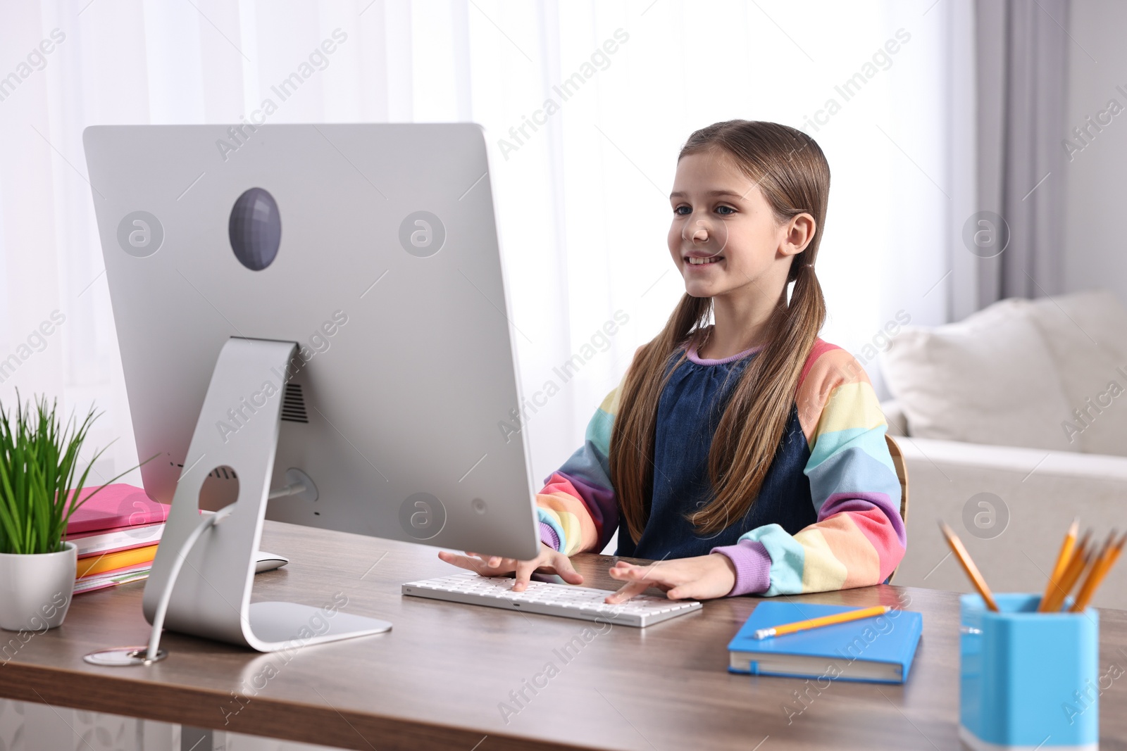 Photo of E-learning. Cute girl using computer during online lesson at table indoors