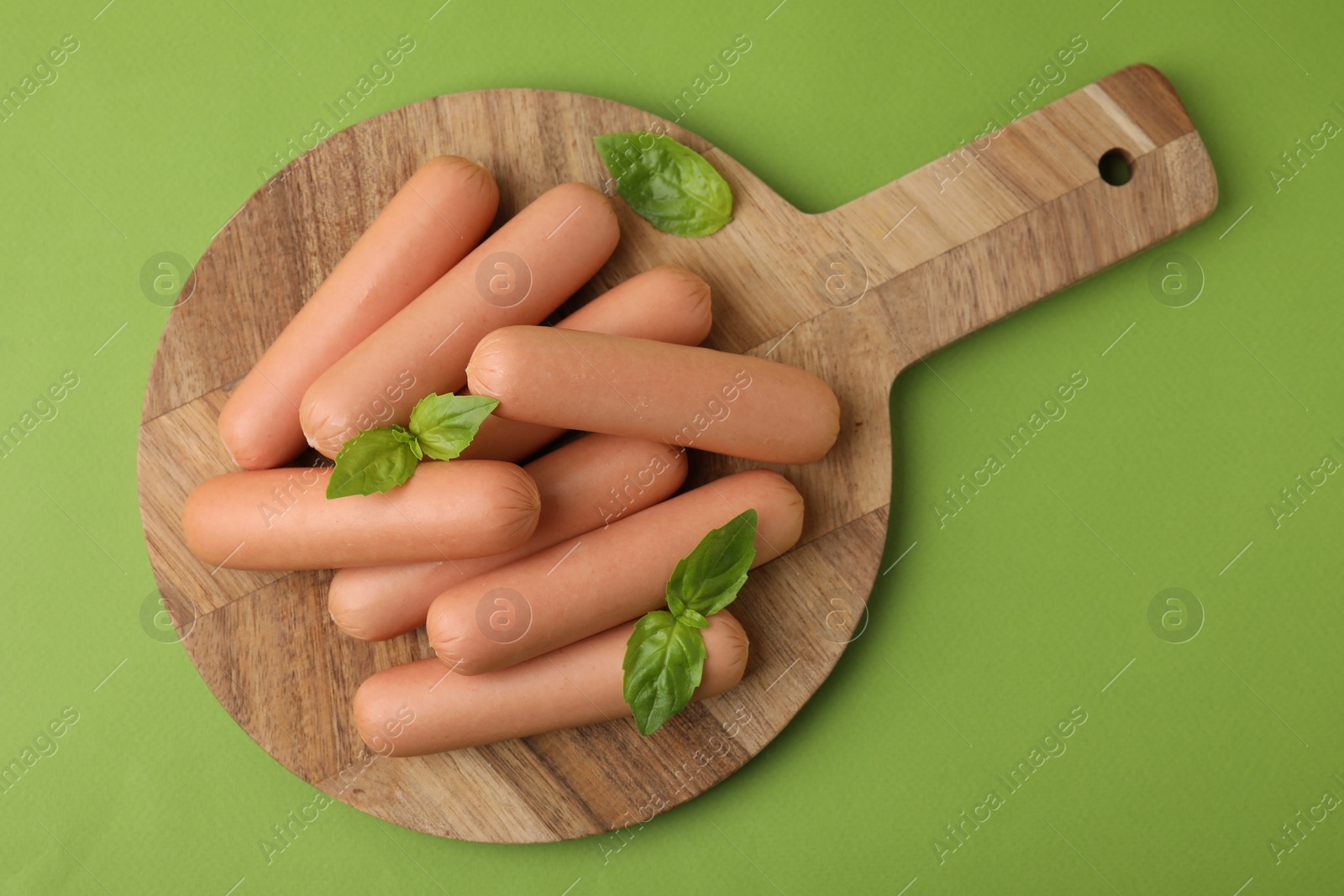 Photo of Delicious boiled sausages and basil on green table, top view