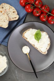 Photo of Pieces of bread with cream cheese, basil leaves and tomatoes on gray textured table, flat lay