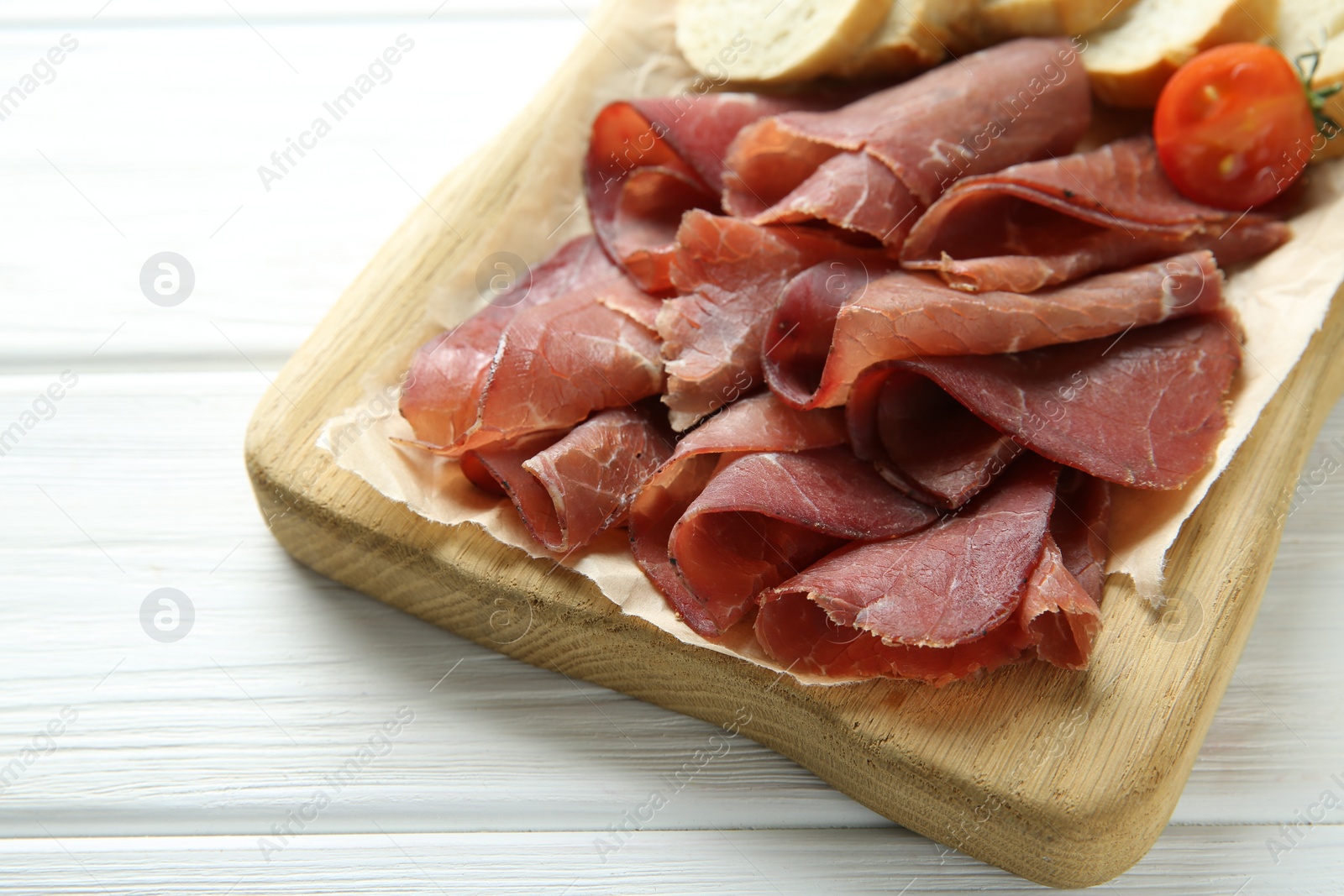 Photo of Board with delicious bresaola on white wooden table, closeup. Space for text