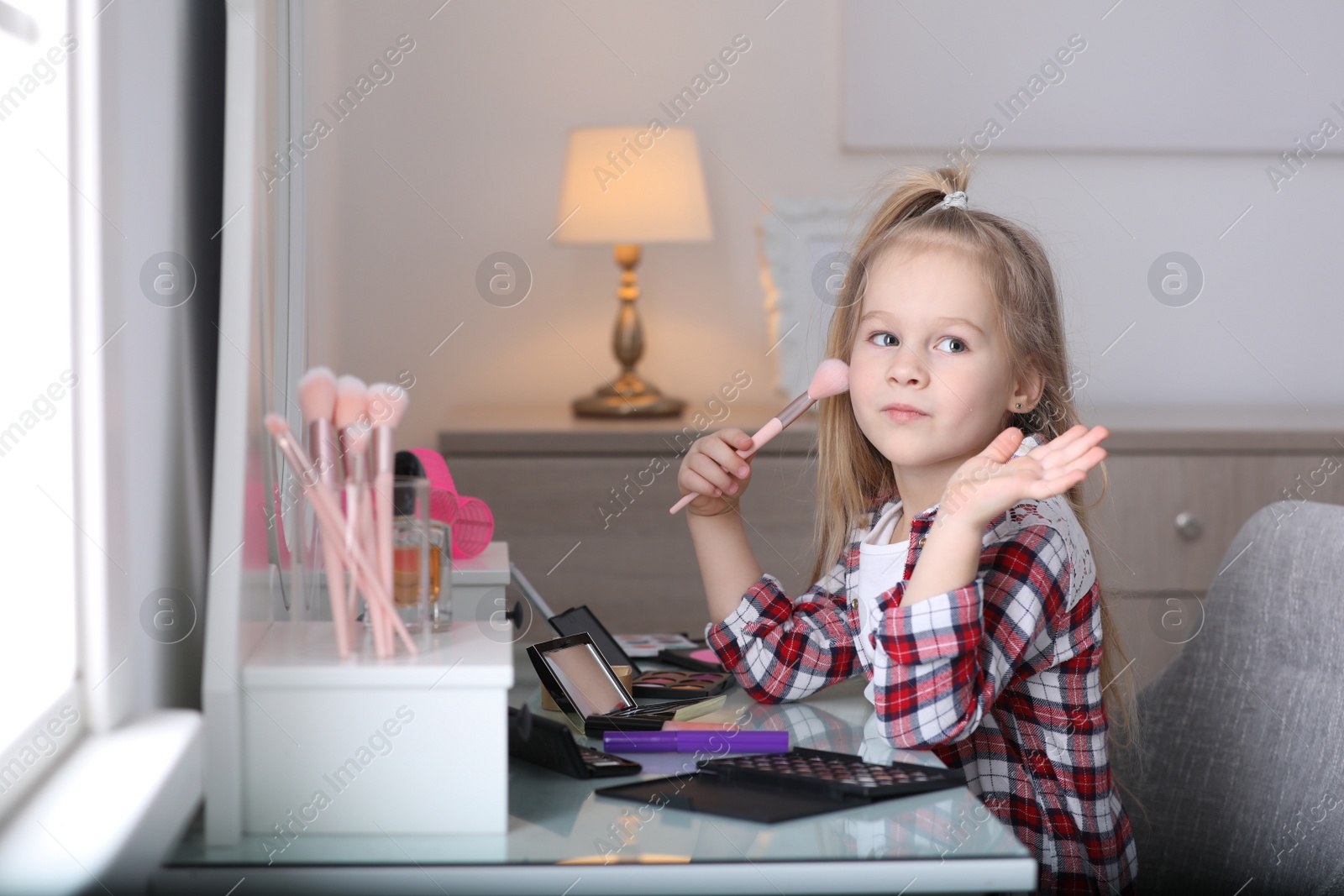 Photo of Adorable little girl applying makeup at dressing table indoors