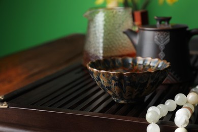 Photo of Cup with freshly brewed pu-erh tea and prayer beads on wooden tray, closeup. Space for text
