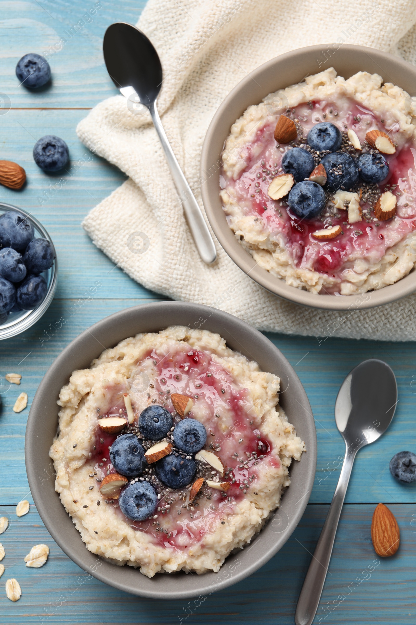 Photo of Tasty oatmeal porridge with toppings served on light blue wooden table, flat lay