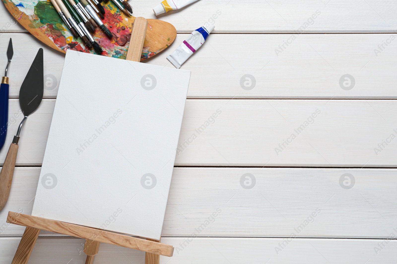 Photo of Blank canvas, tools and paints on white wooden table, flat lay. Space for text