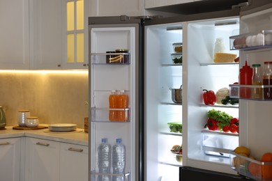 Open refrigerator full of different products in kitchen