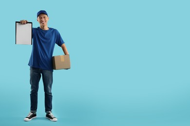 Photo of Happy courier with parcel and clipboard on light blue background. Space for text