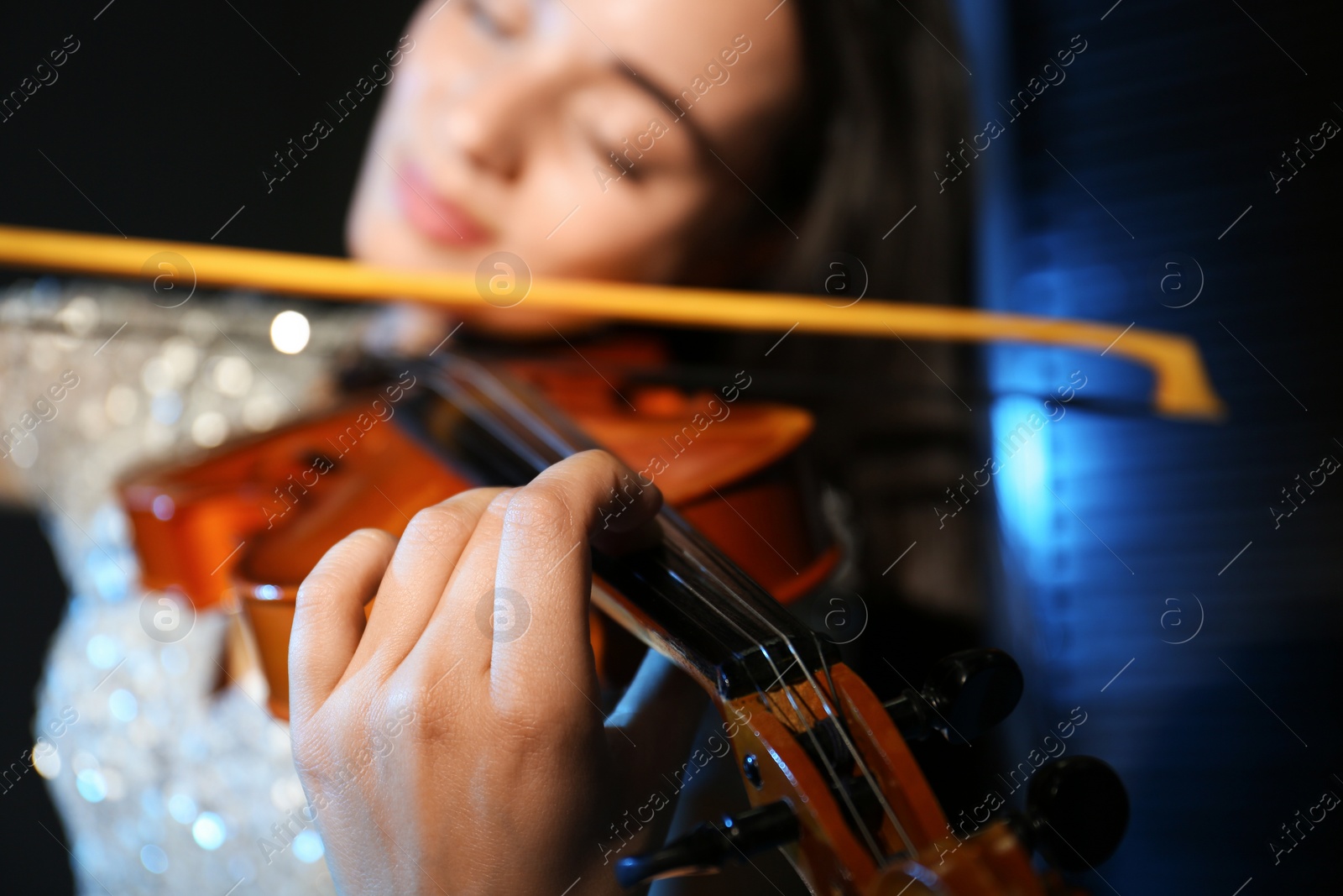 Photo of Beautiful young woman playing violin in dark room, closeup