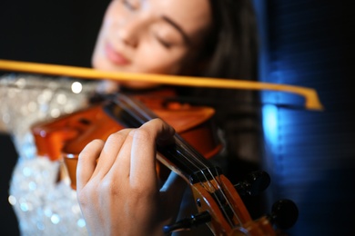 Photo of Beautiful young woman playing violin in dark room, closeup