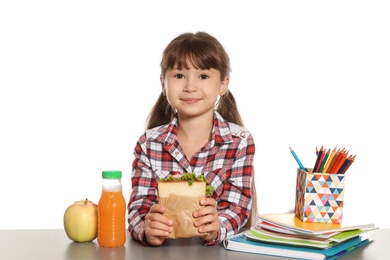 Schoolgirl with healthy food and backpack sitting at table on white background