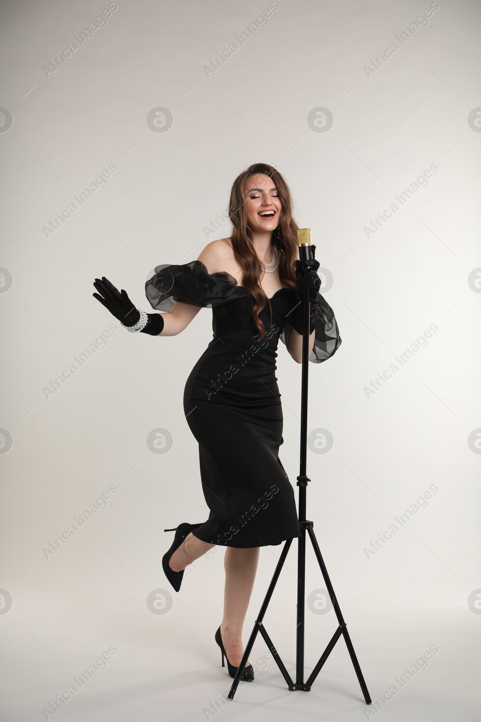 Photo of Beautiful young woman in stylish dress with microphone singing on light grey background