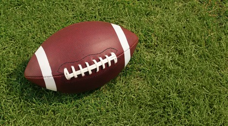 Photo of American football ball on green grass. Space for text