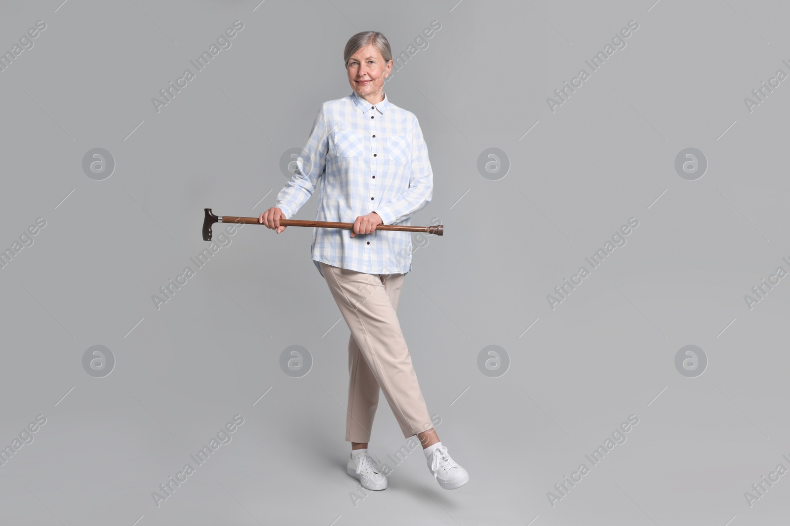 Photo of Senior woman with walking cane on gray background