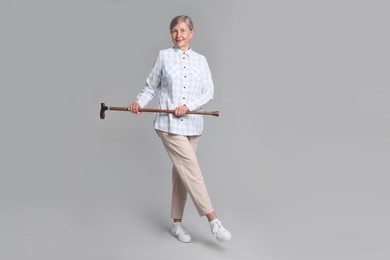 Senior woman with walking cane on gray background