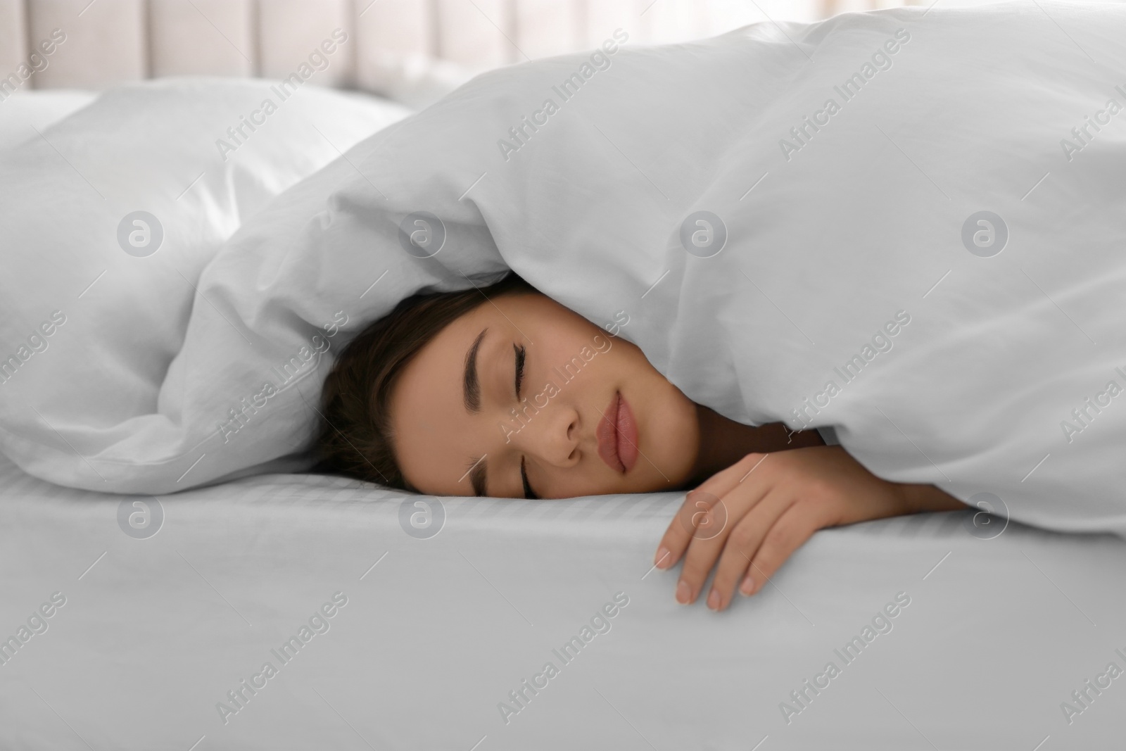 Photo of Young woman covered with warm white blanket sleeping in bed at home