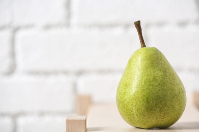 Ripe pear on wooden shelf against blurred background. Space for text