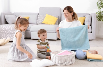 Photo of Housewife with children folding freshly washed towels in room