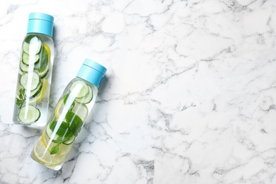 Bottles of refreshing water with cucumber, lemon and mint on white marble table, flat lay. Space for text