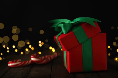 Photo of Red Christmas gift box with candy canes on wooden table. Space for text