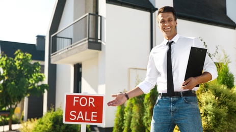 Photo of Real estate agent near red sign in front of house outdoors