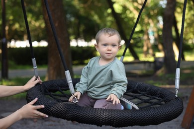 Nanny and cute little boy on swing in park