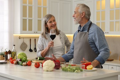 Photo of Happy senior couple cooking together in kitchen. Woman with glass of wine near her husband