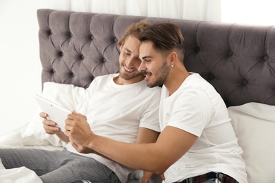 Happy gay couple with tablet computer on bed at home