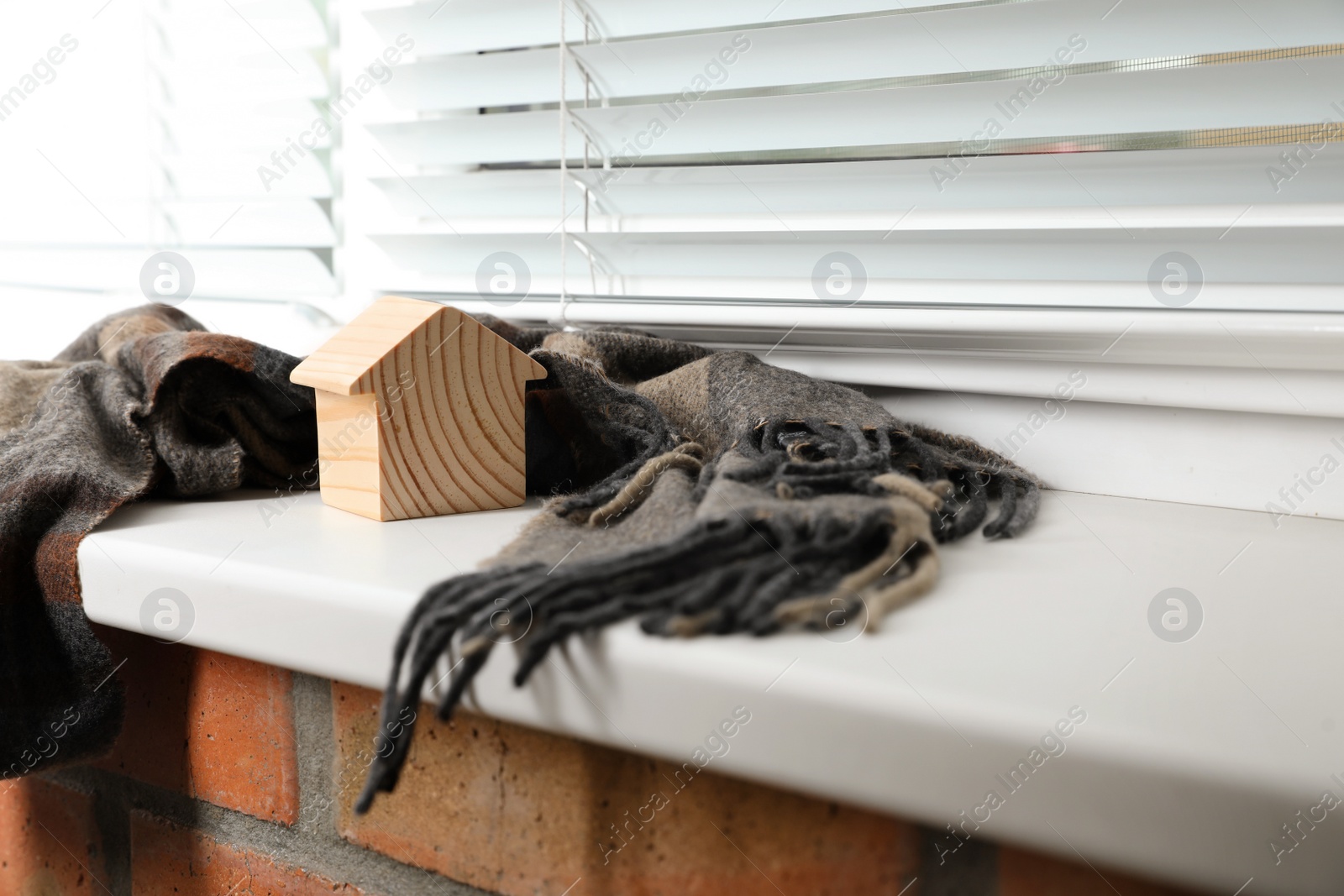 Photo of Wooden house model and scarf on window sill indoors, space for text. Heating efficiency