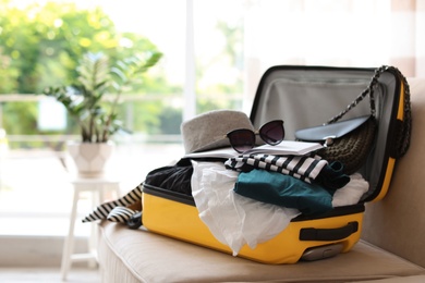 Photo of Open yellow suitcase with different clothes packed for journey at home