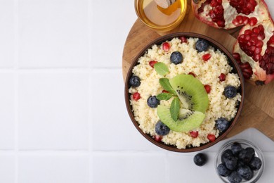 Photo of Bowl of tasty couscous with kiwi, blueberries, pomegranate and honey on white table, flat lay. Space for text