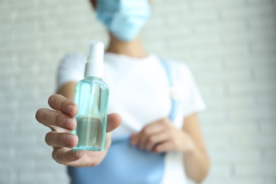 Photo of Woman holding hand sanitizer against blurred background, closeup. Personal hygiene during COVID-19 pandemic
