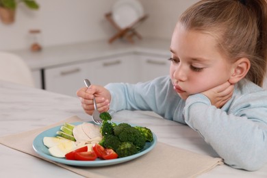 Photo of Cute little girl refusing to eat dinner in kitchen