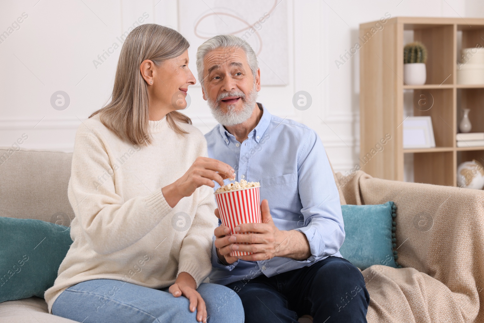 Photo of Happy senior couple with popcorn on sofa indoors