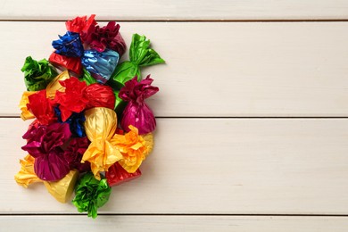 Photo of Candies in colorful wrappers on beige wooden table, flat lay. Space for text