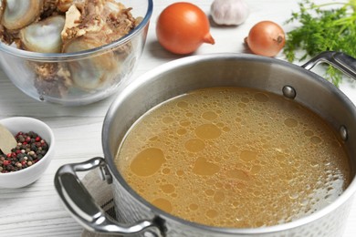 Delicious homemade bone broth and ingredients on white wooden table, closeup view