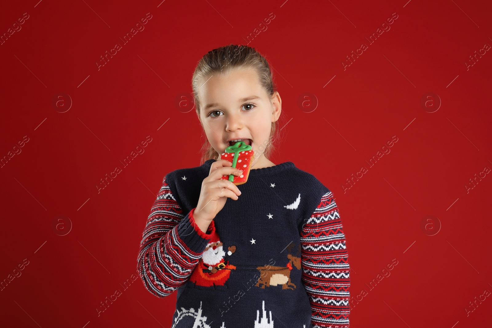 Photo of Cute little girl with Christmas gingerbread cookie on red background