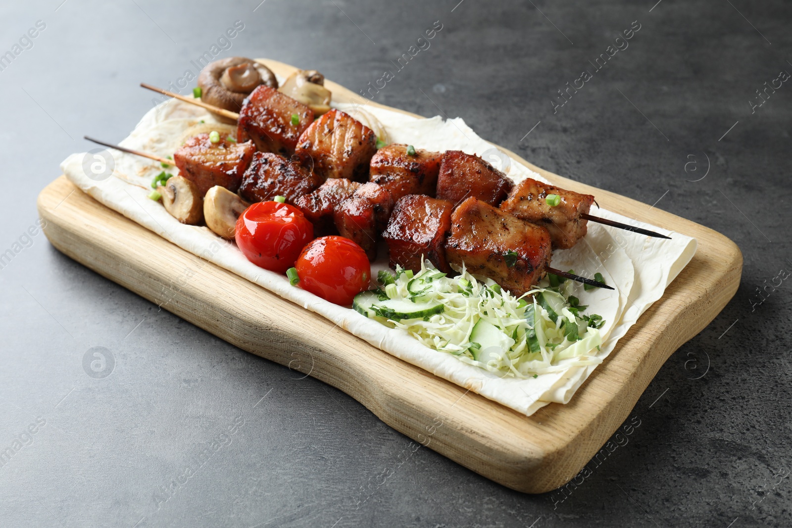 Photo of Delicious shish kebabs with vegetables and lavash on grey table