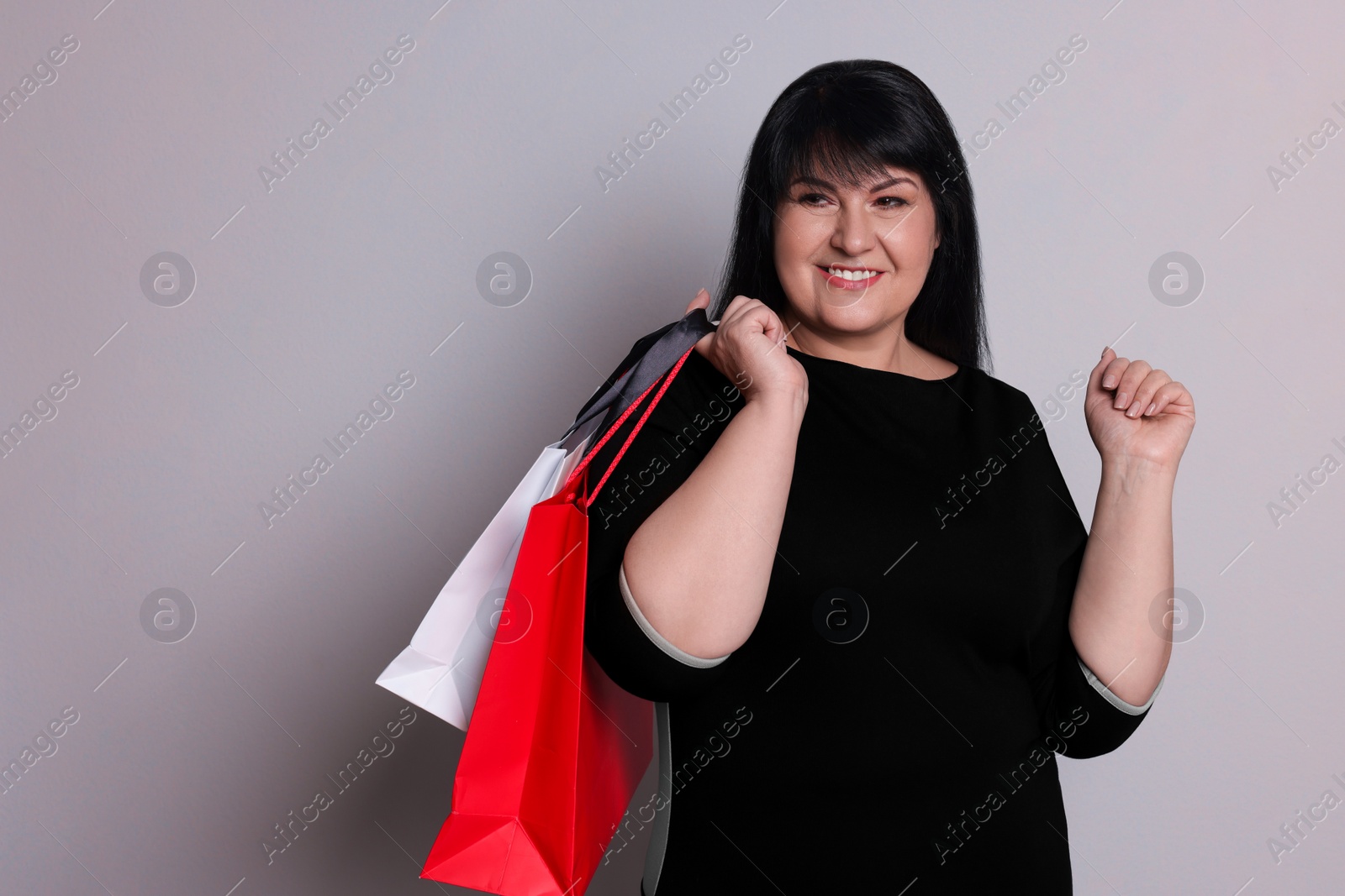 Photo of Beautiful overweight mature woman with shopping bags on light grey background. Space for text