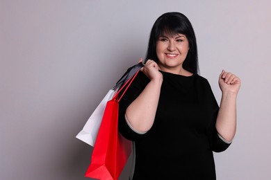 Photo of Beautiful overweight mature woman with shopping bags on light grey background. Space for text