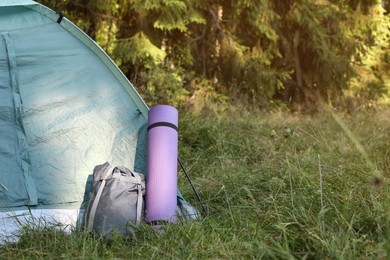 Sleeping bag and mat near camping tent outdoors, space for text