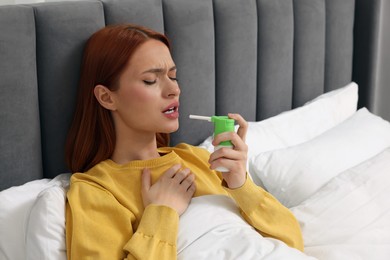 Young woman using throat spray in bed