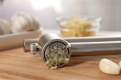 Photo of Garlic press with mince and clove on wooden table, closeup