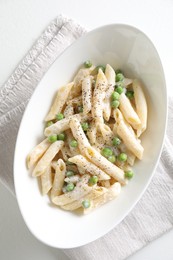 Delicious pasta with green peas and creamy sauce in bowl on white table, top view