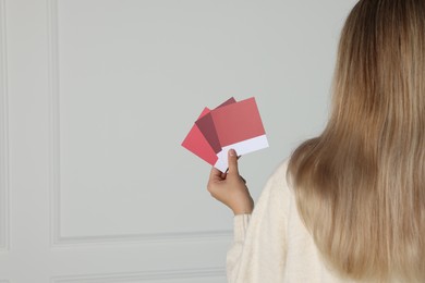 Photo of Woman choosing paint shade for wall indoors, focus on hand with color sample cards. Interior design