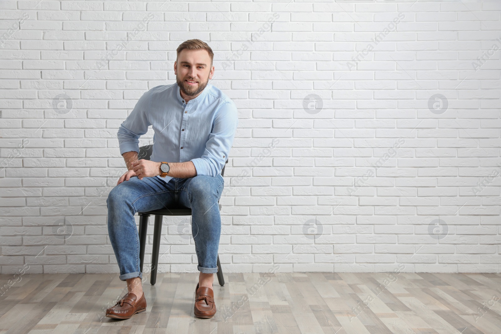 Photo of Young man sitting on chair near white brick wall in office, space for text