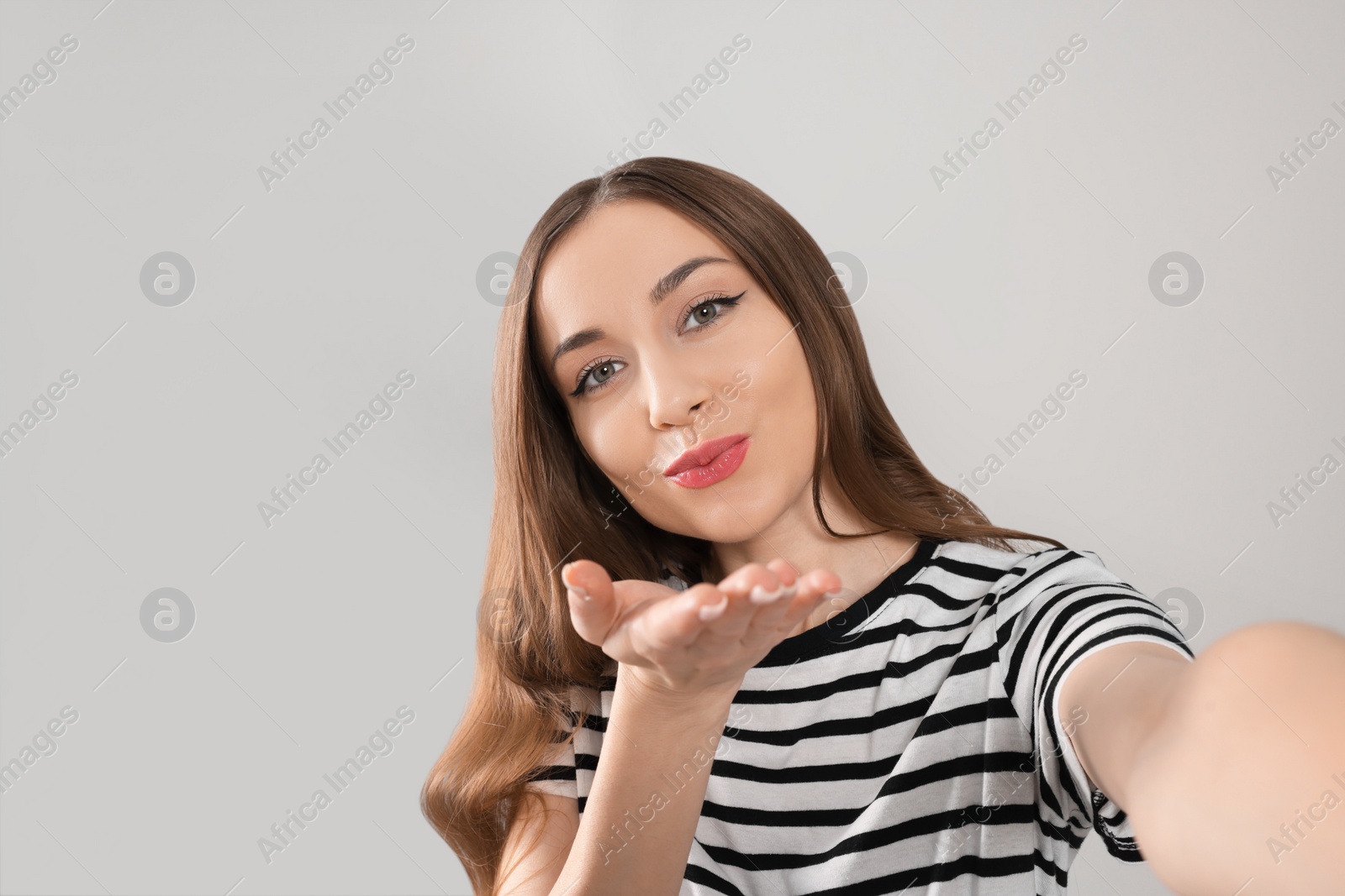 Photo of Beautiful young woman blowing kiss while taking selfie on light grey background, space for text