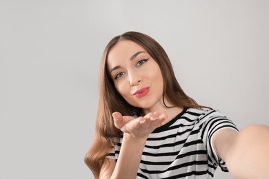 Photo of Beautiful young woman blowing kiss while taking selfie on light grey background, space for text