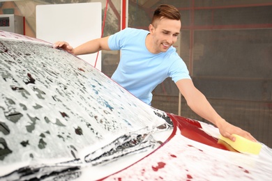 Photo of Young man cleaning vehicle with sponge at self-service car wash