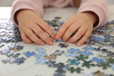 Photo of Little child playing with puzzles at table, closeup