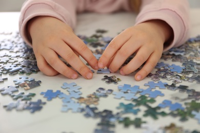 Little child playing with puzzles at table, closeup