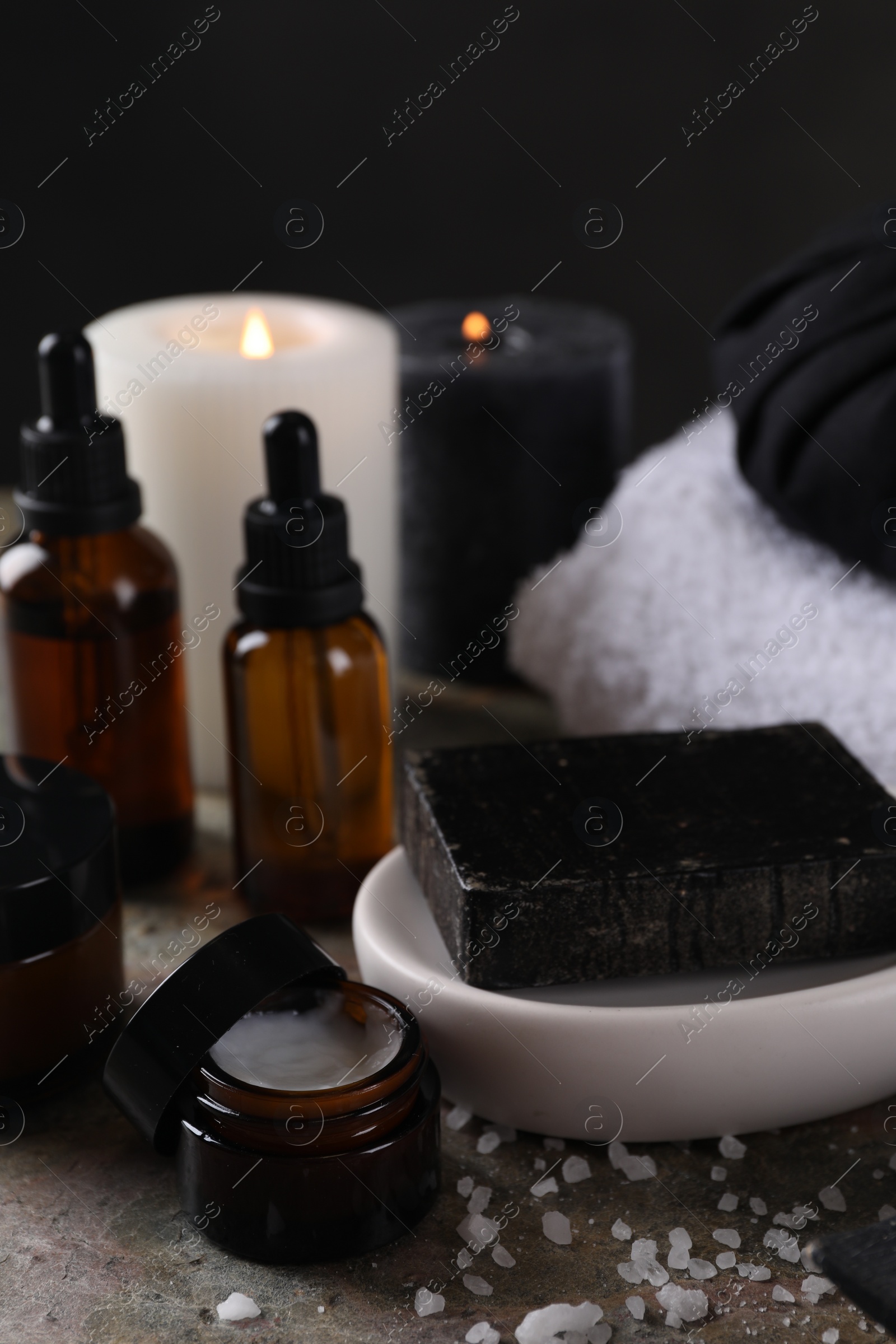 Photo of Spa composition. Black soap bar, sea salt, jar of cream and towels on table